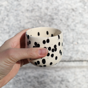 Latte coffee mug Black Dots made of stoneware with black and white glaze held in the hand.
