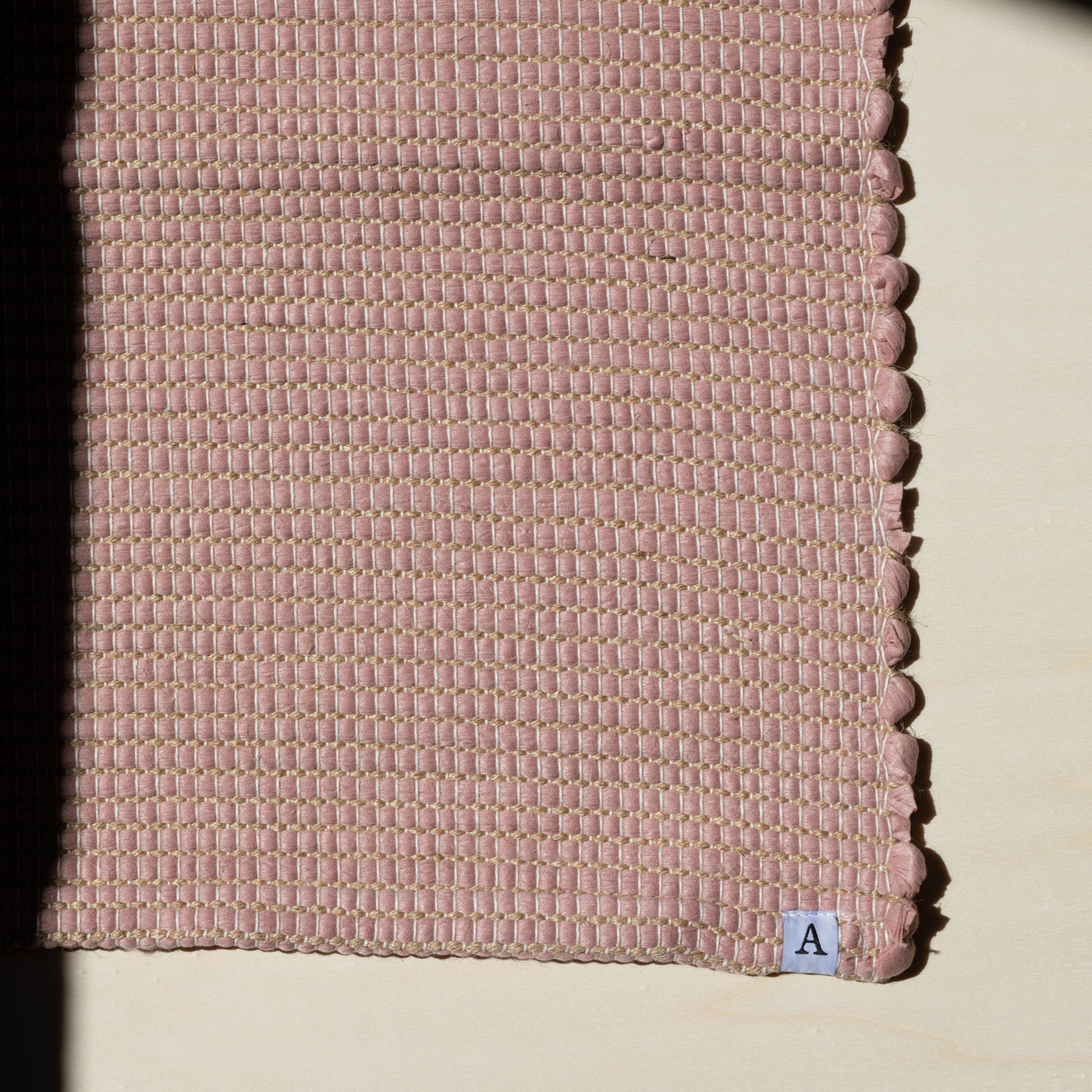 Close-up d'un petit tapis 60x90cm en vieux rose avec du jute entrelacé tissé à la main à partir de coton upcycling au Portugal