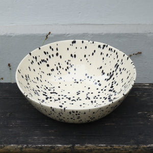 Beige salad bowl speckled with black spots of color on a woody background