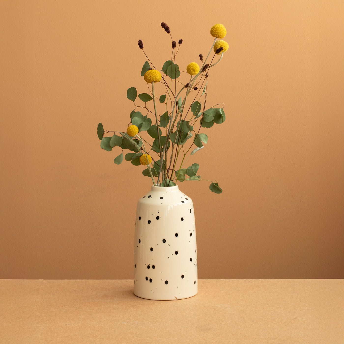 Vase Bottle de couleur beige à points noirs contenant un strass floral vert-jaune sur fond de terre cuite chaude 