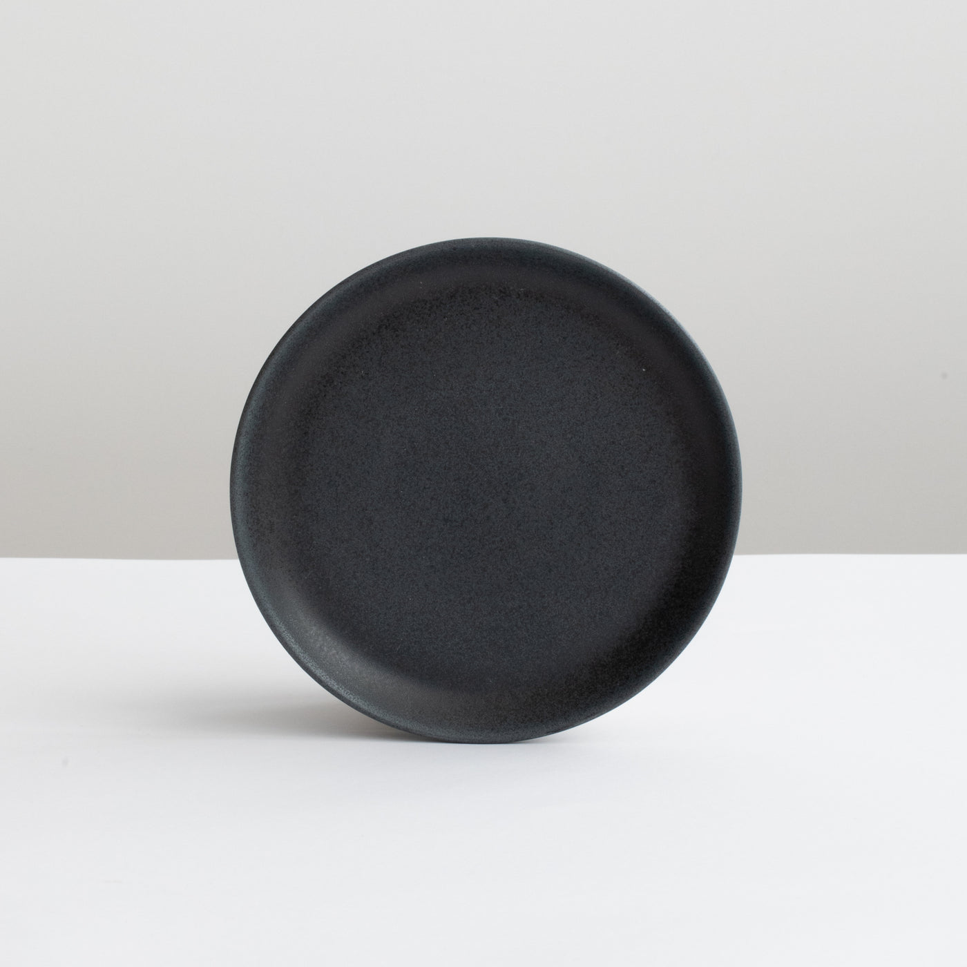 Matt black round saucer with a diameter of 15.5 cm against a light gray background