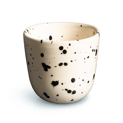 Beige Kaffeetasse mit schwarzen Punkten vor weissem Hintergrund freigestellt