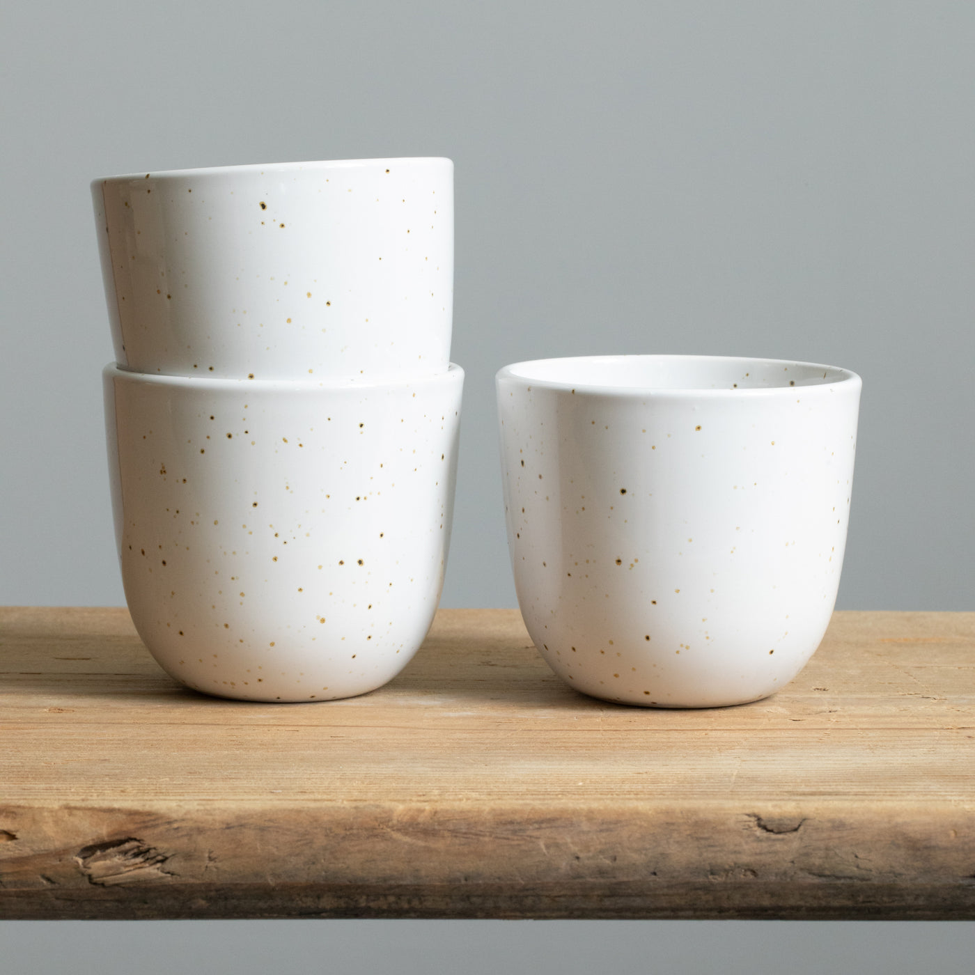 Two stacked cappuccino mugs in a shiny white color with fine golden sprinkles