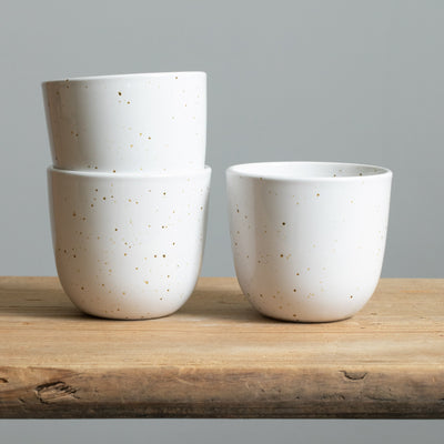Two stacked cappuccino mugs in a shiny white color with fine golden sprinkles