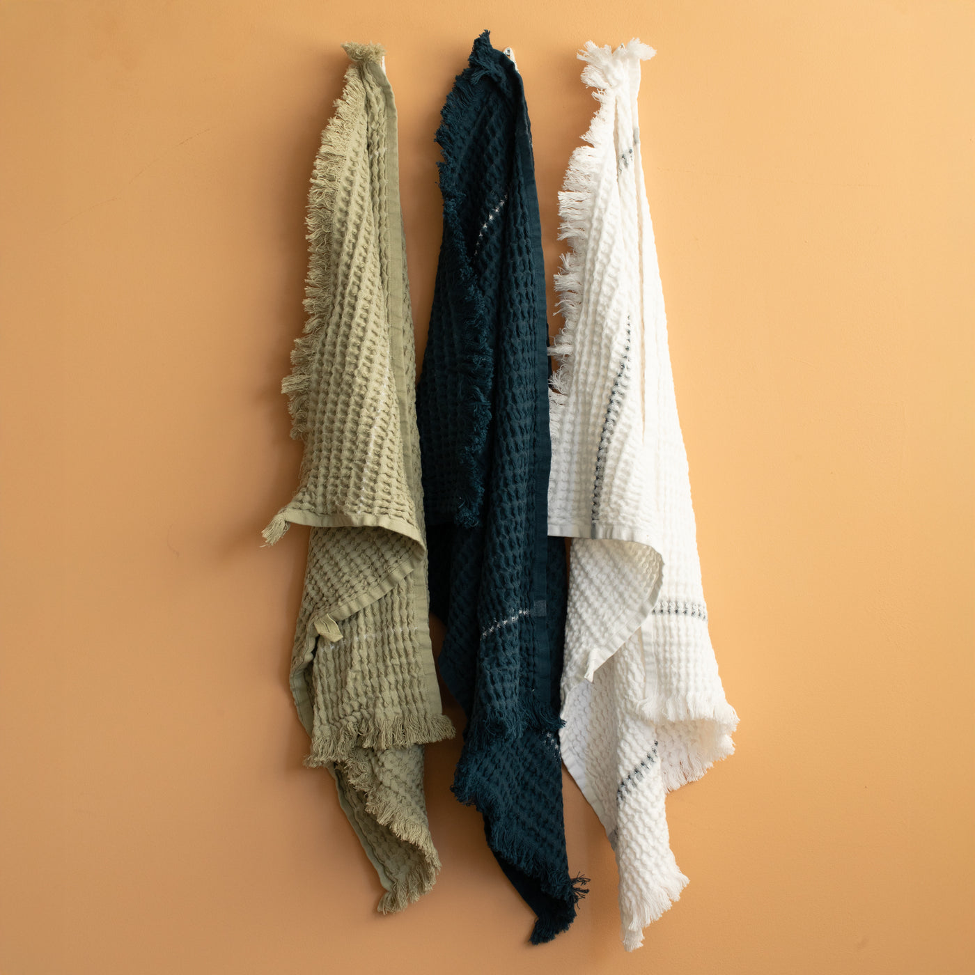 Towel set with waffle pattern in blue, green and white hung in front of terracotta colored wall