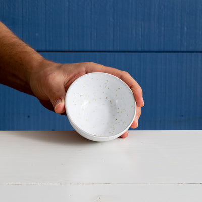 Petit bol rond en céramique émaillée blanche à pois dorés, tenu debout par une main.