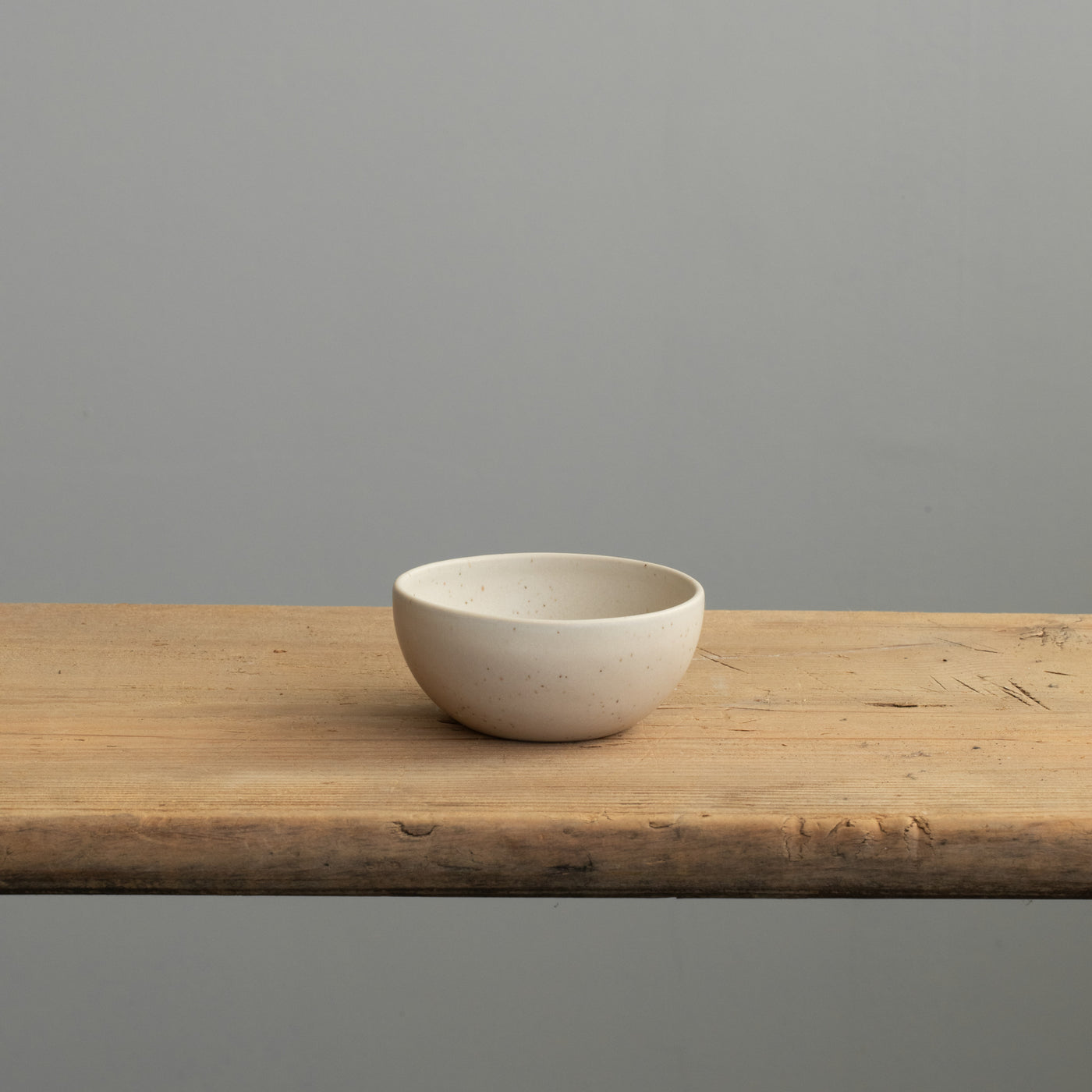 Vue de face d'un petit bol beige en émail mat posé sur une table en bois