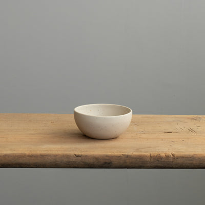 Vue de face d'un petit bol beige en émail mat posé sur une table en bois