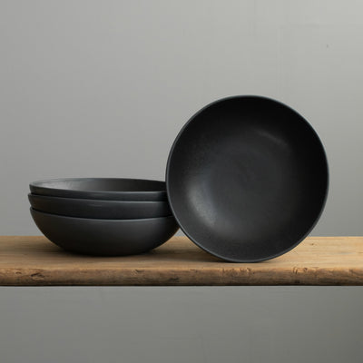 Assiette de pâtes noire mate empilée en grès sur une table en bois