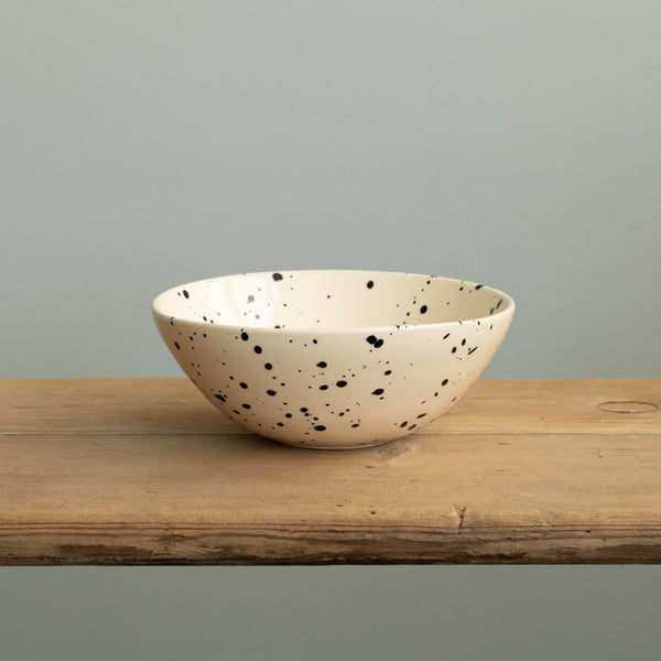 A small bowl in Puglia style with black dots and a slightly open rim on a wooden table