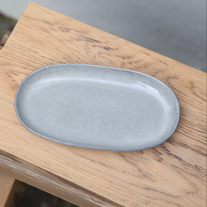 Hellgrauer 22cm langer ovaler Untertassenteller von oben gesehen auf einem Holzbrett