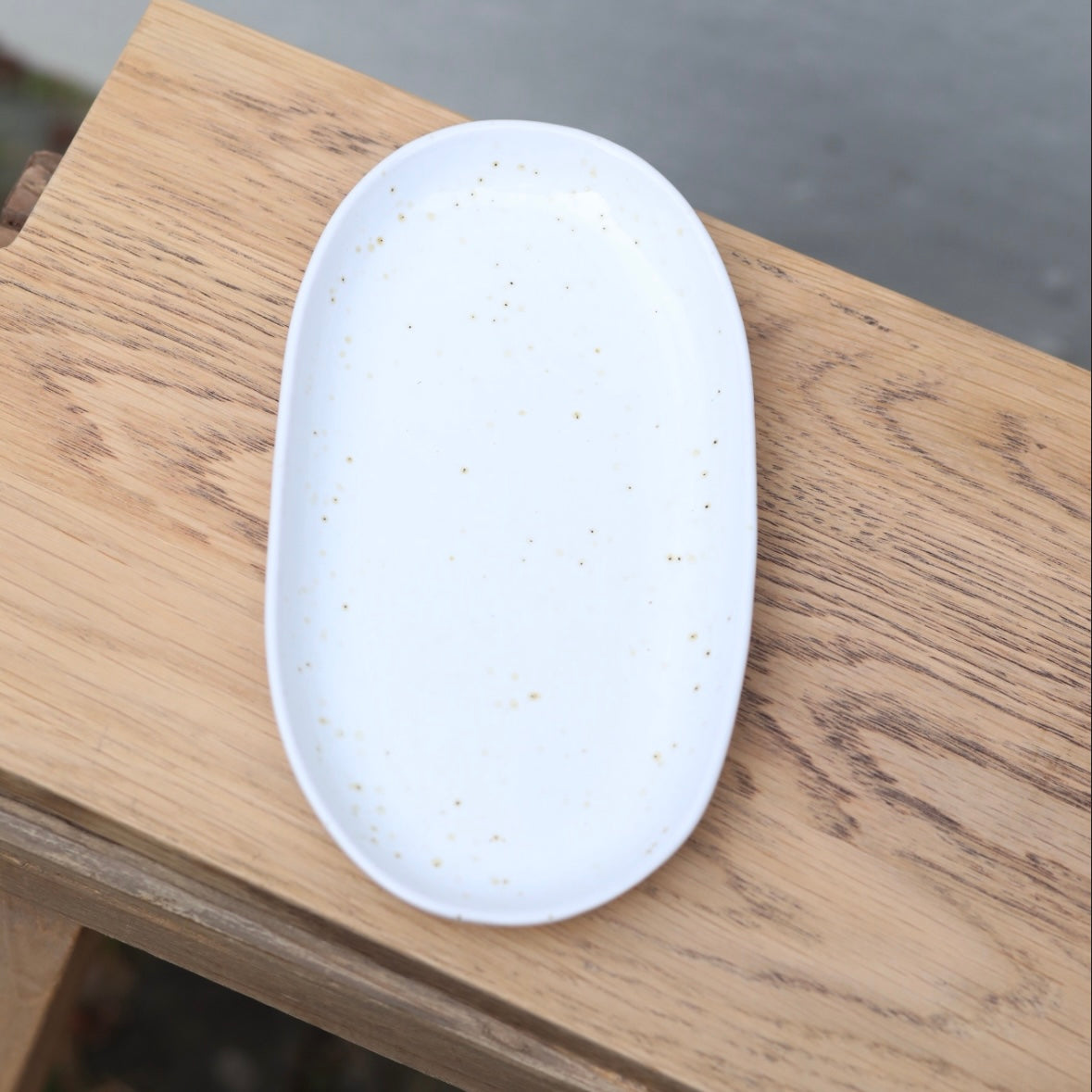 Von oben fotografierter weisser 22cm langer ovaler Teller mit feinen braunen Sprenklern perfekt als Unterteller