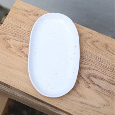 Von oben fotografierter weisser 22cm langer ovaler Teller mit feinen braunen Sprenklern perfekt als Unterteller