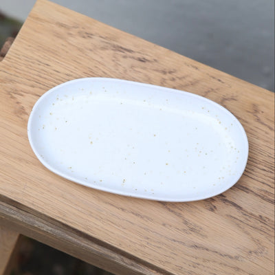Weisse Untertasse in ovaler Form mit weisser reaktiver Glasur und goldenen Punkten