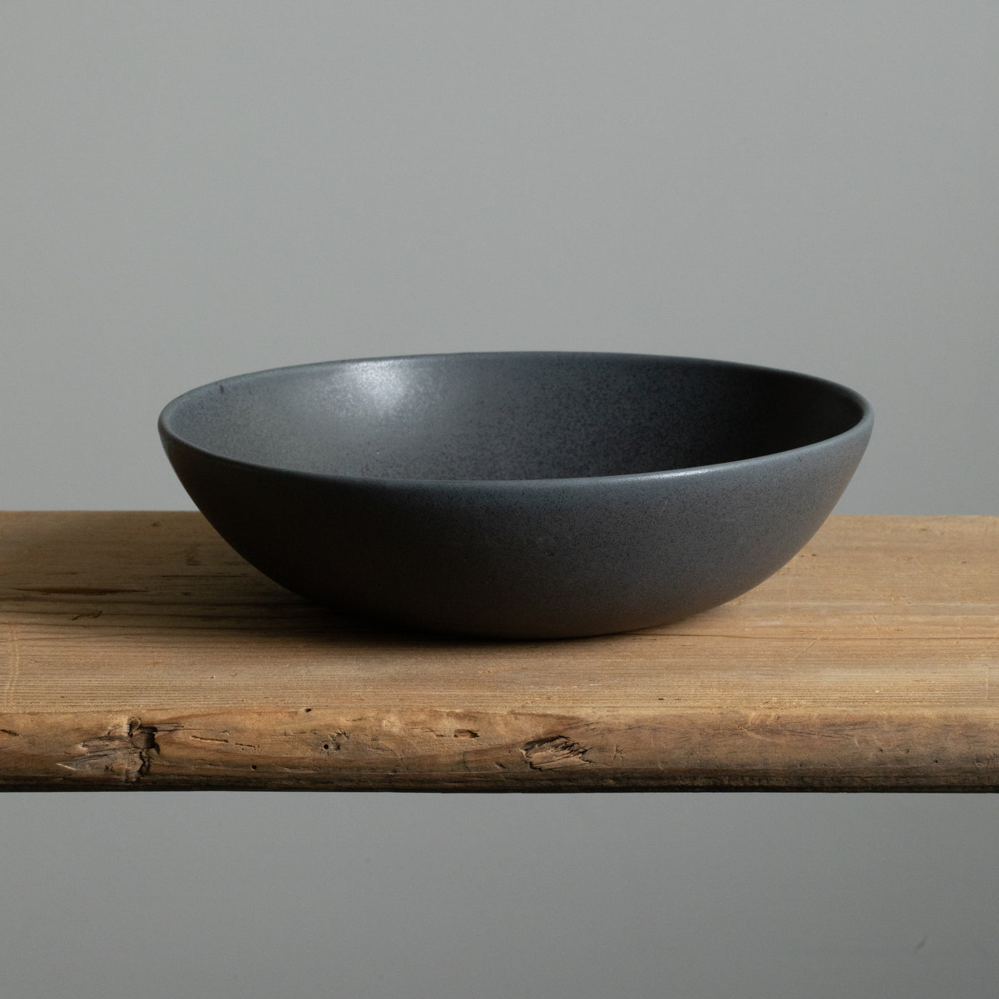 Assiette creuse noire mate pour pâtes, vue de face sur une table en bois