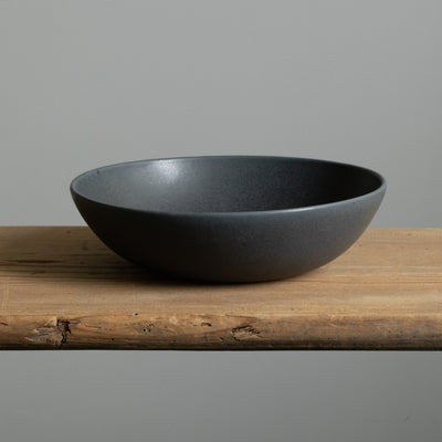 Assiette creuse noire mate pour pâtes, vue de face sur une table en bois