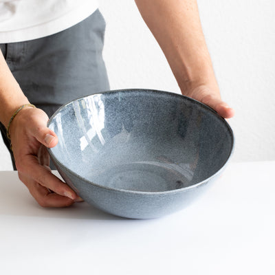 Blue deep salad bowl held by hands on a white table 
