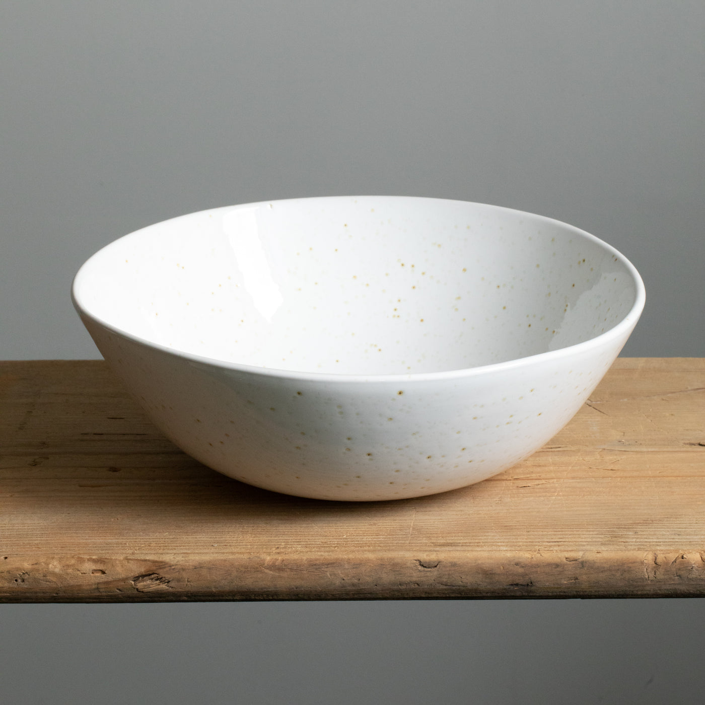 Large white salad bowl with golden-brown splashes of color freestanding on a wooden table