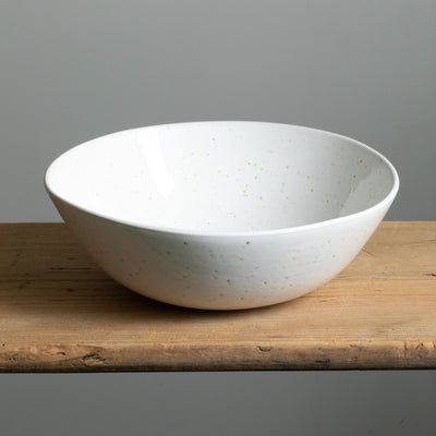 Large white salad bowl with golden-brown splashes of color freestanding on a wooden table