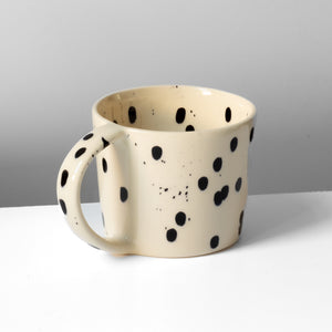 Grande tasse à thé avec anse beige à pois noirs sur fond gris