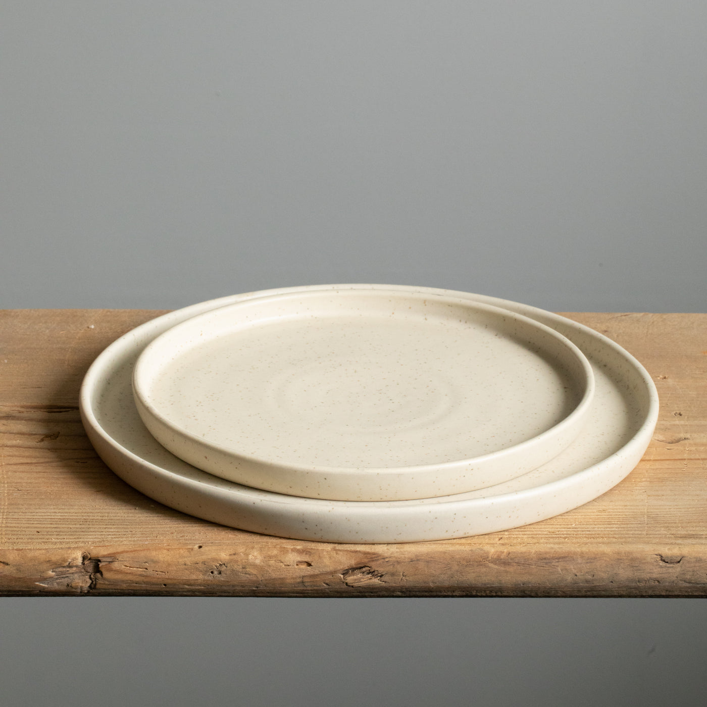 Large and small plate placed on top of each other with angled rim and matt beige glaze